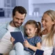 father, mother and young girl sitting on a sofa looking at an iPad the child is holding.