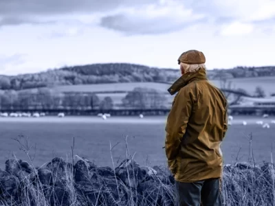 farmer with his back to the camera looking our over a field with sheep in and hills behind.