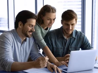 Three people looking at a laptop in an office.
