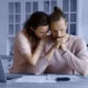 Unhappy young woman supporting worried husband looking at documents on a kitchen counter.